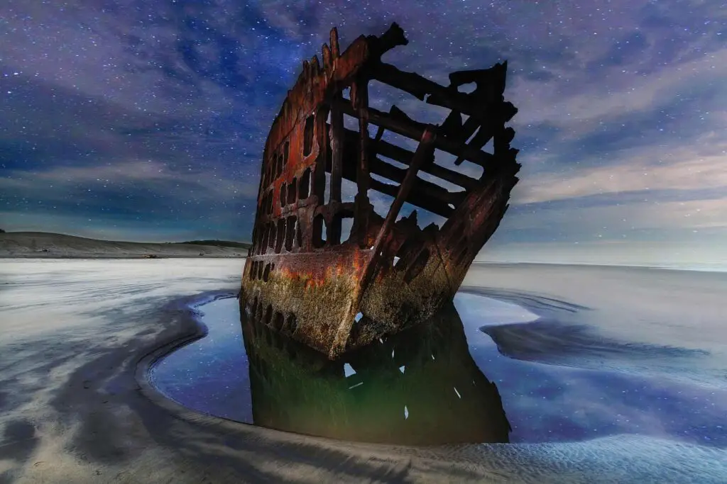 The Peter Iredale shipwreck under starlight, reflecting in a pool of water.
