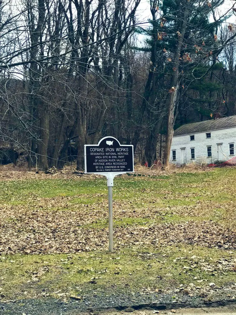 National historical register sign in the grass before a white clapboard building designating the Copake IronWorks as a National HIstoric Site.