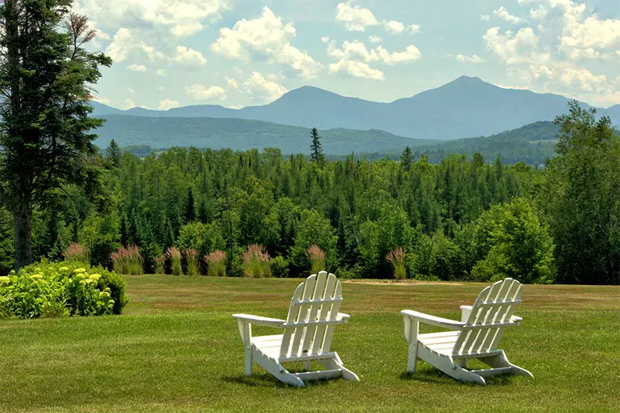 Adirondack chairs sit on grass in front of mountainous view at a Summer vacation destination in the USA, New Hampshire