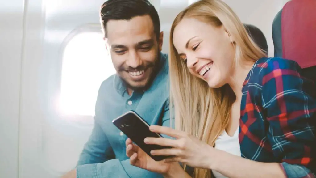 Happy airline passengers looking at a phone while enjoying a flight on a top airline