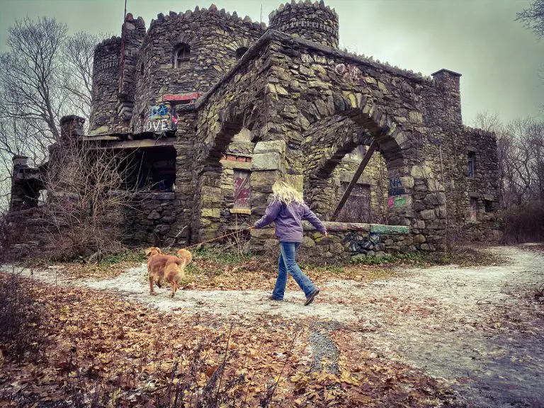 Young woman and golden retriever walk in front of Hearthstone Castle ruins