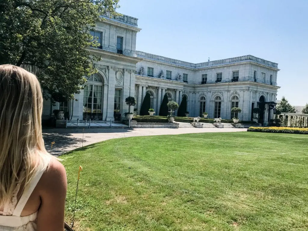 Young blond woman visiting New England stares at old Newport Mansion.
