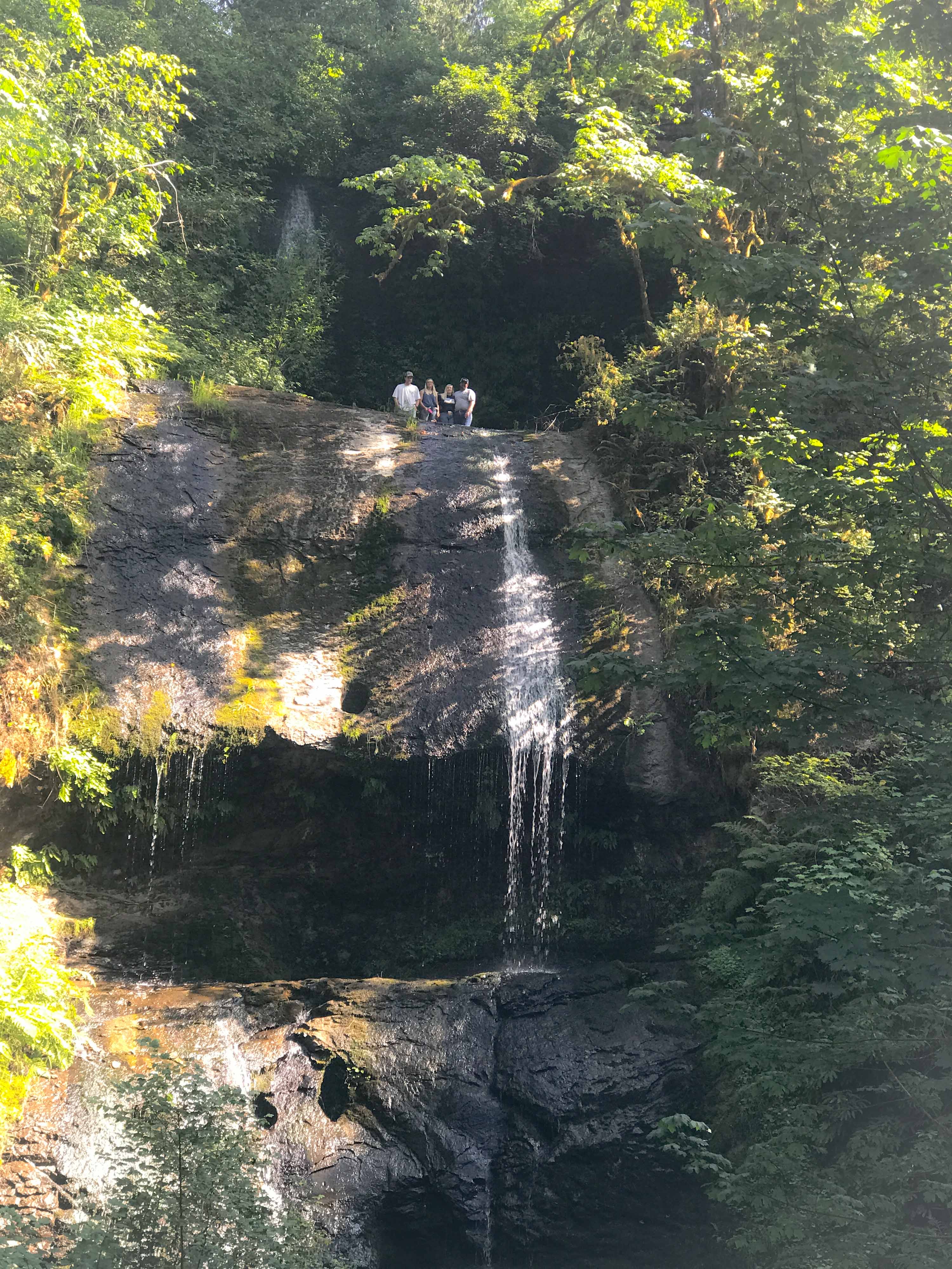 A group of people stand on top of trickling Royal Terrace Falls in the Summer