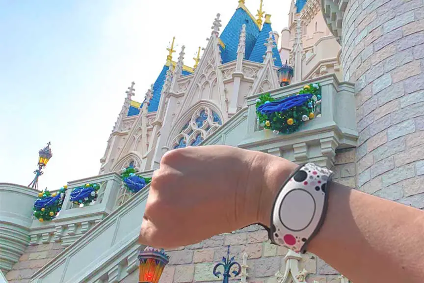 Woman holding up arm with MagicBand in front of Cinderella's Castle at Magic Kingdom.