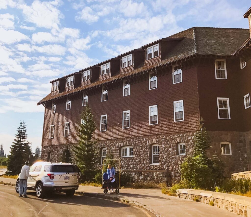 Crater Lake Lodge with car in front and visitor taking in the views