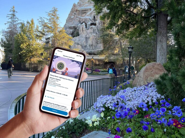 hand holding smartphone showing Disneyland Genie+ reservation in front of Matterhorn Bobsleds, a Disneyland Genie+ ride.