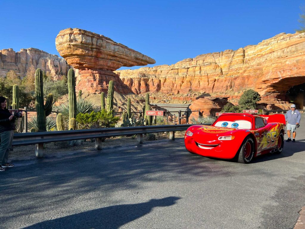 Lightning McQueen drives down a road in a dessert landscape with sculpted rock formations, one thing you can do at Disneyland that you can't do at Disney World.