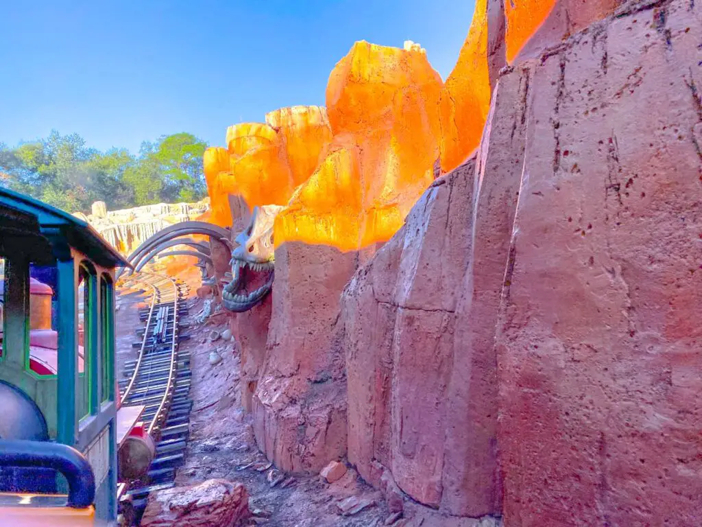 Big Thunder Mountain Railroad train dips beneath a dinosaur skeleton in Magic Kingdom in a day.