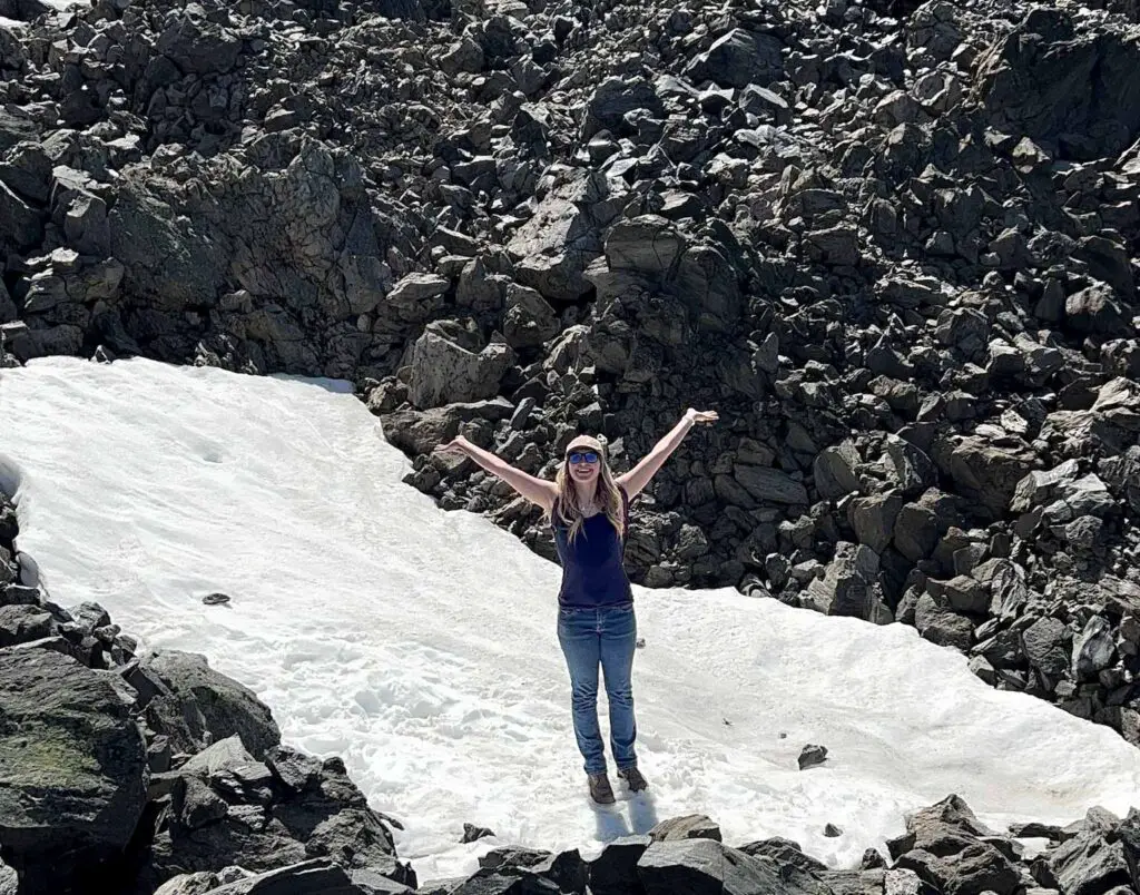 Young blond woman stands in snow before a pile of obsidian at Newberry Volcanic Monument Big Obsidian Flow