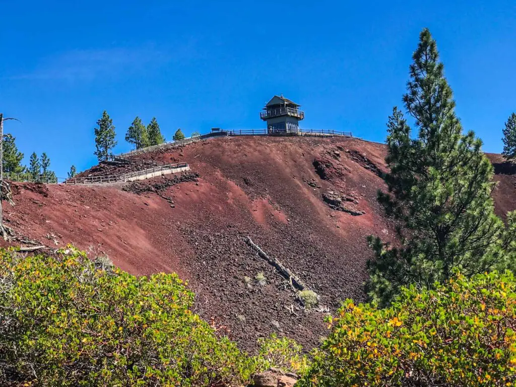 fire tower rises from the red brown rock atop lava butte cinder cone at Newberry volcanic monument in Oregon