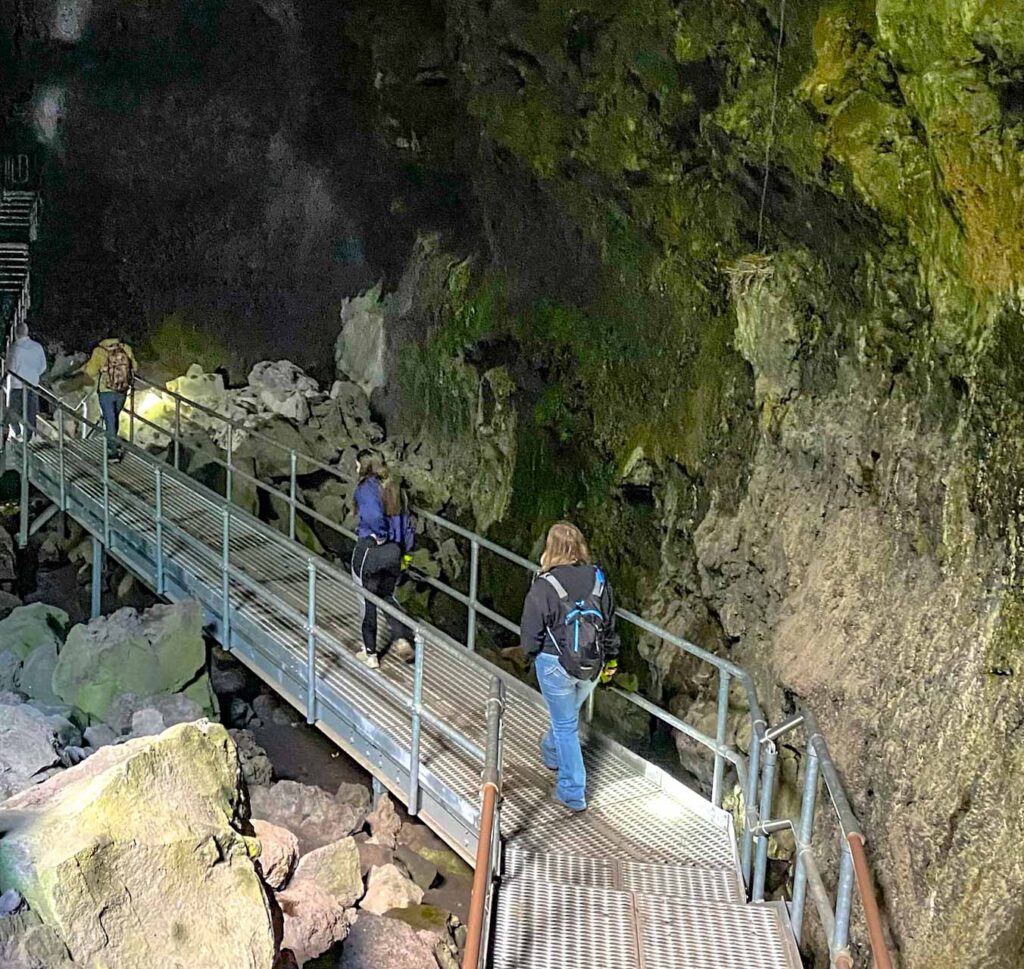 Women walking a metal boardwalk, leading into Lava River Cave Oregon.