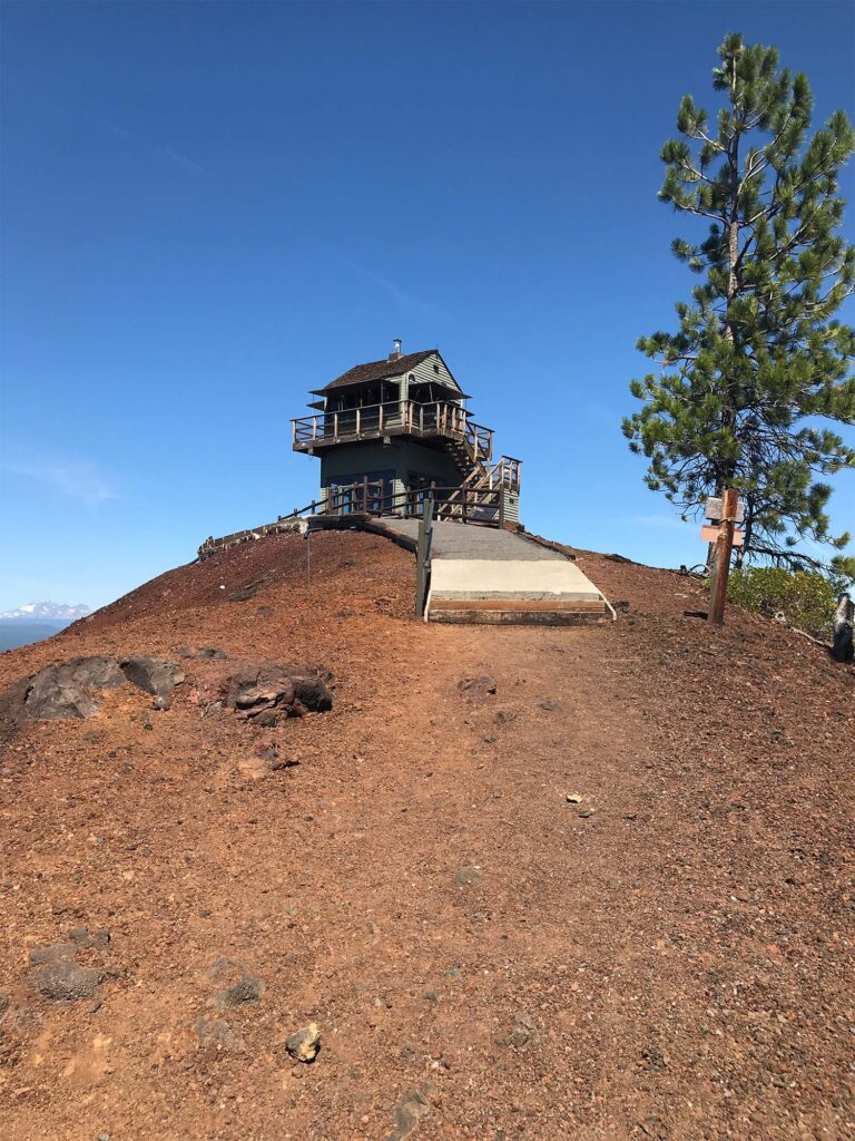 fire tower rises from the red brown rock atop lava butte cinder cone at Newberry volcanic monument in Oregon