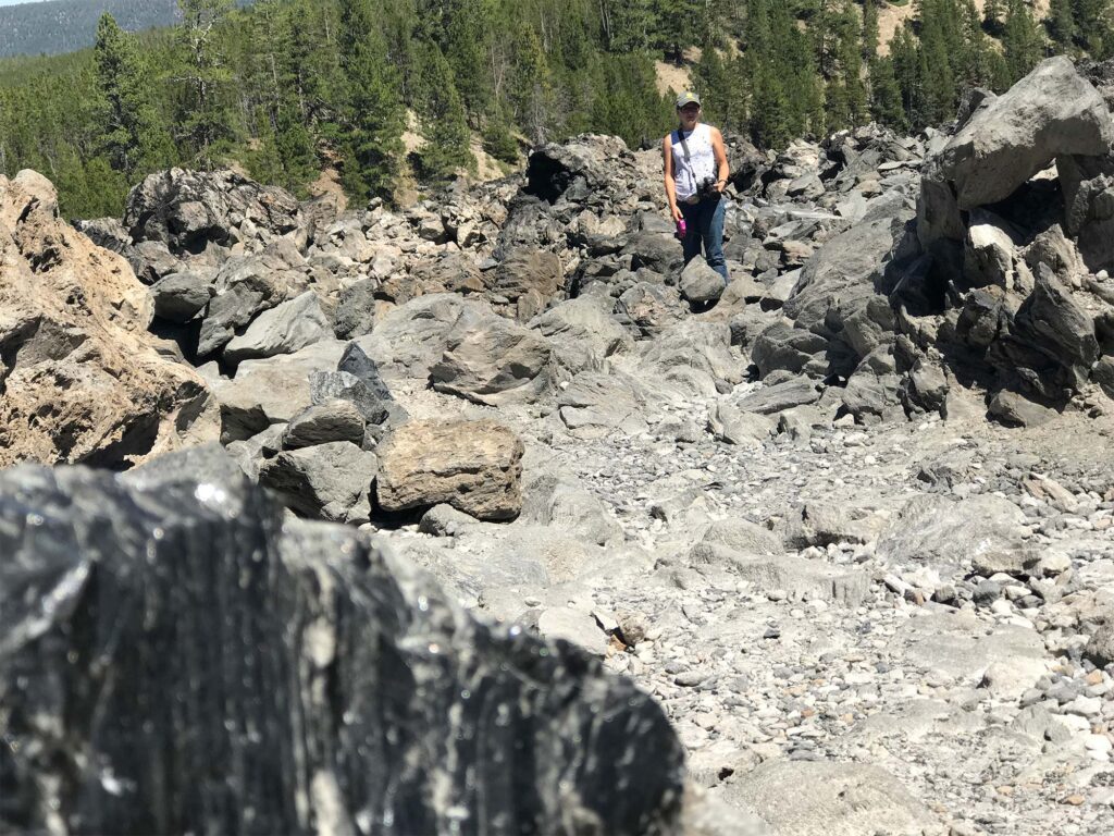 Young blond woman stands in snow before a pile of obsidian at Newberry Volcanic Monument Big Obsidian Flow