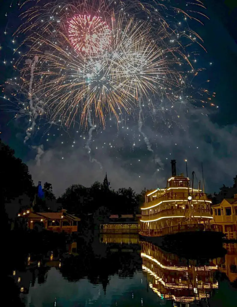 Fireworks erupt over the Mark Twain Riverboat Magic Kingdom at night.
