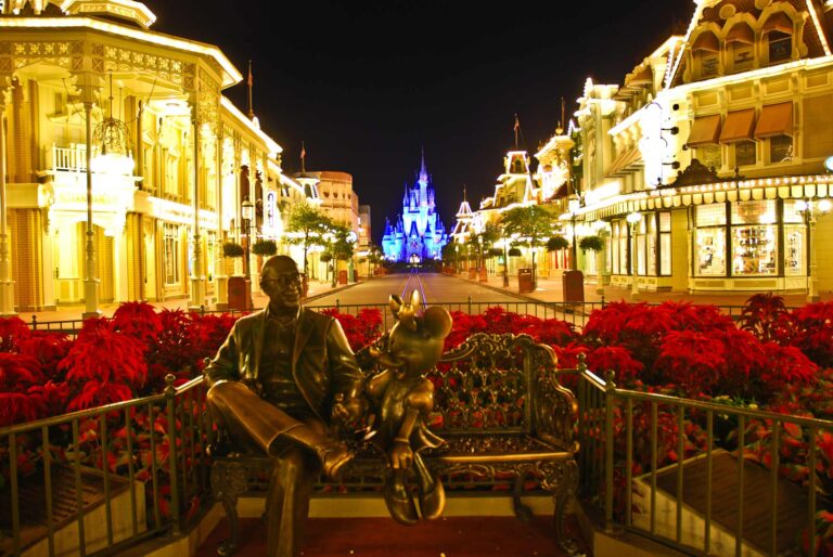 Walt Disney with Minnie Mouse, sitting on a bench in front of a lit up Main Street-Disney World at night