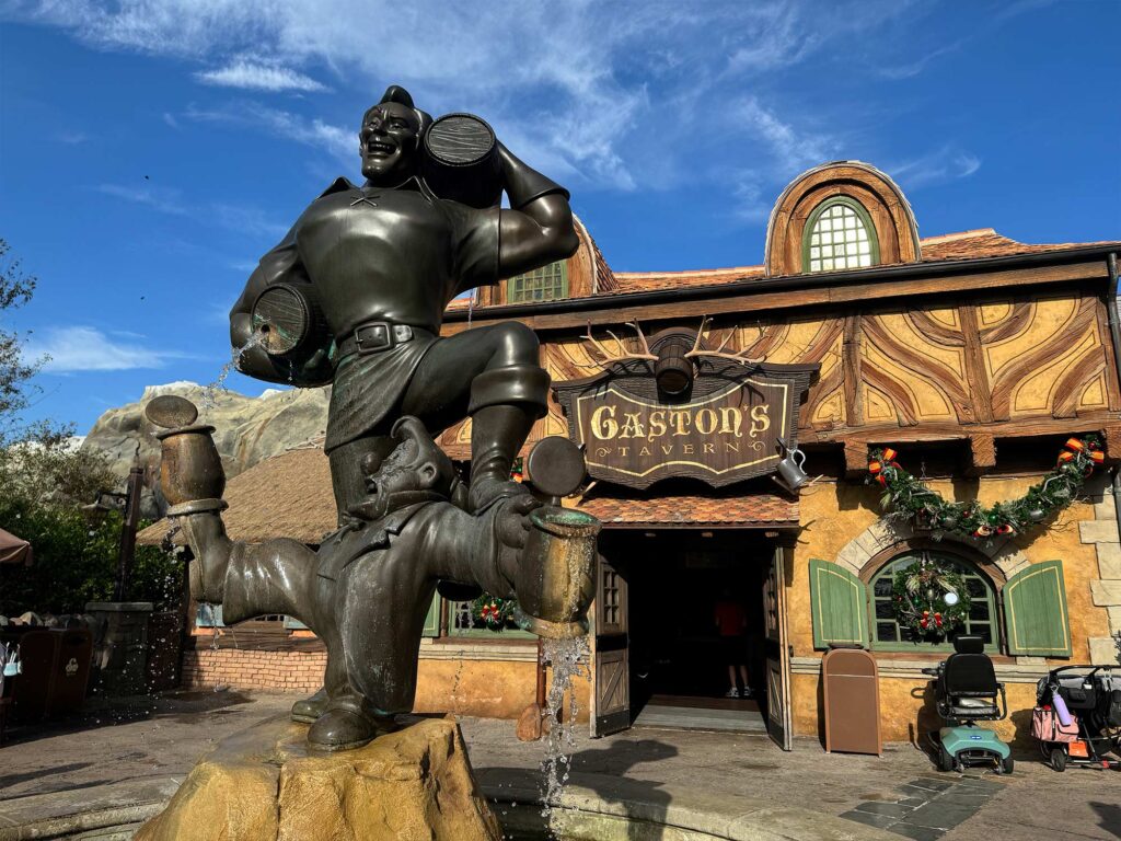 Exterior of Gaston's Tavern, featuring Gaston statue holding a large barrel and stepping on Lefou. One of the best Magic Kingdom restaurants for a snack.