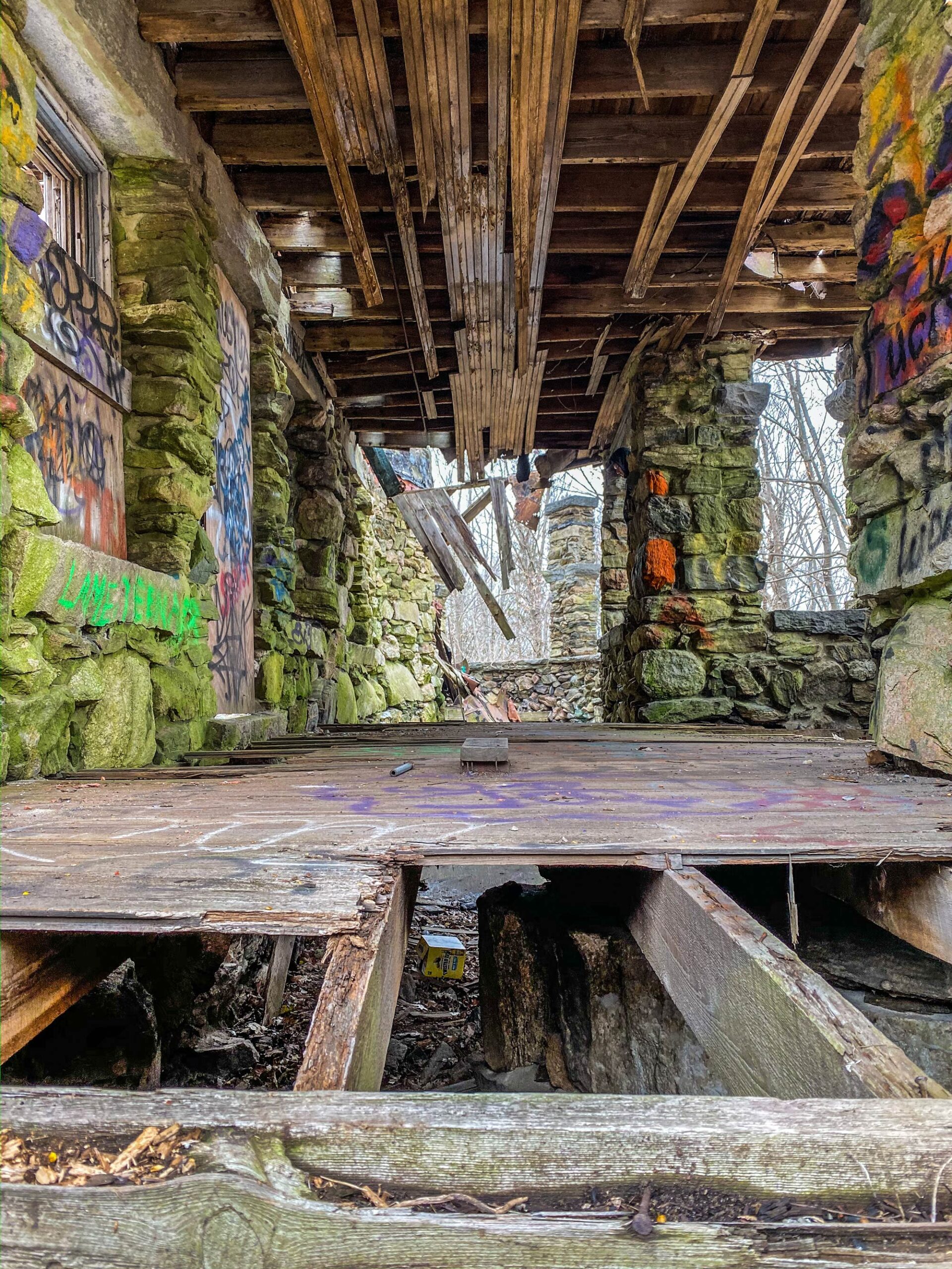 missing floorboards on a porch in front of graffiti covered stone walls at Hearthstone Castle