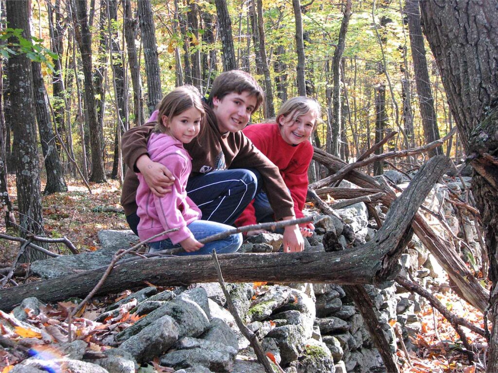 3 children perch on a stone wall in the McLean Game Refuge in Granby, CT