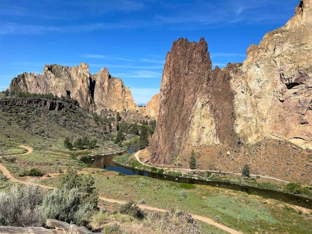 A river winds a course around two enormous rock faces with a green river plain in the foreground at Smith Rock State Park.