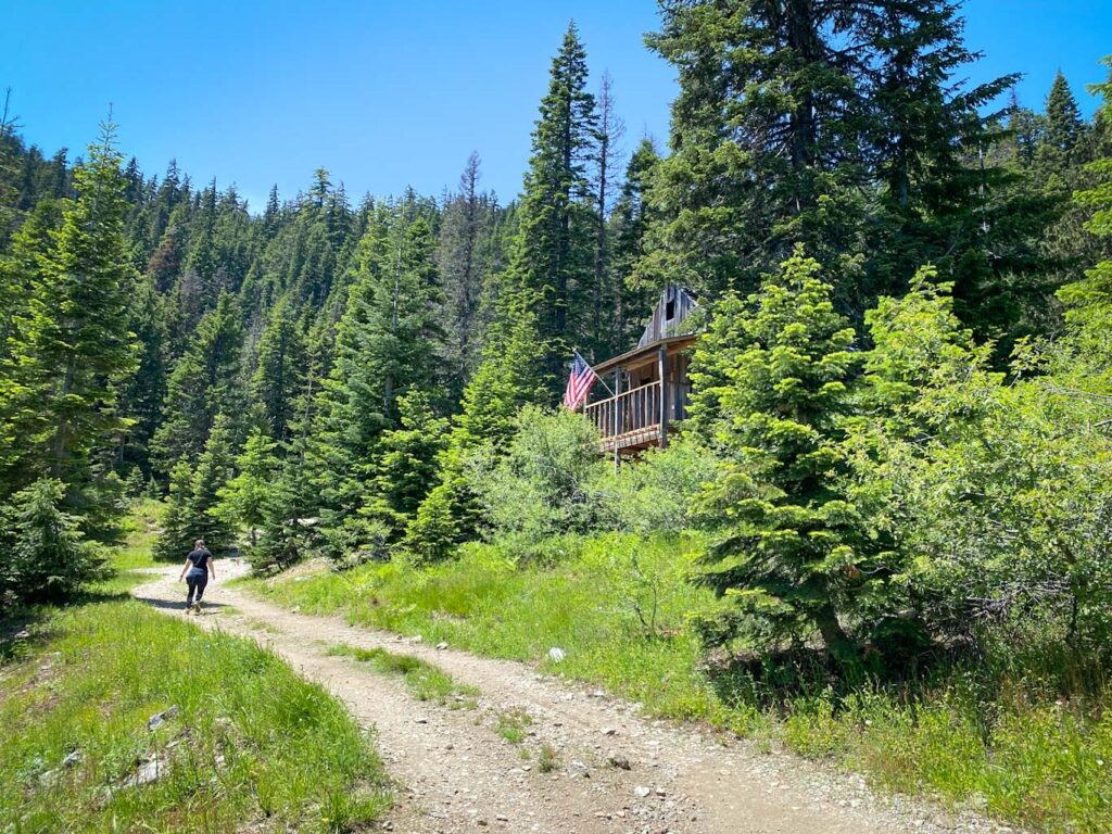 Young woman walks the trail to Bohemia Mine surrounded by evergreens and the abandoned Bohemia Mine post office.