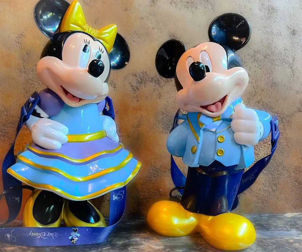 Disney popcorn bucket shaped like Mickey Mouse standing next to a drink sipper shaped like Minnie Mouse, both in Disney World 50th anniversary garb.