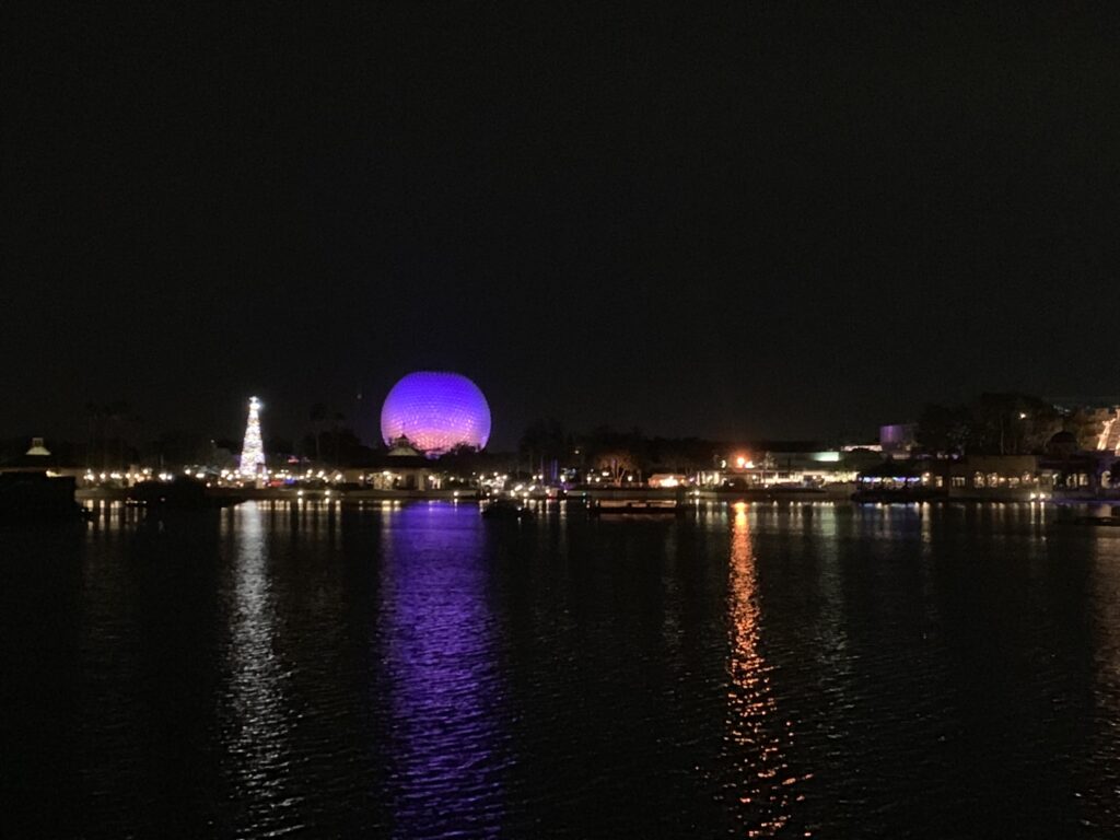 Spaceship Earth lit in purple light beside a shimmering tree during a Disney World Christmas