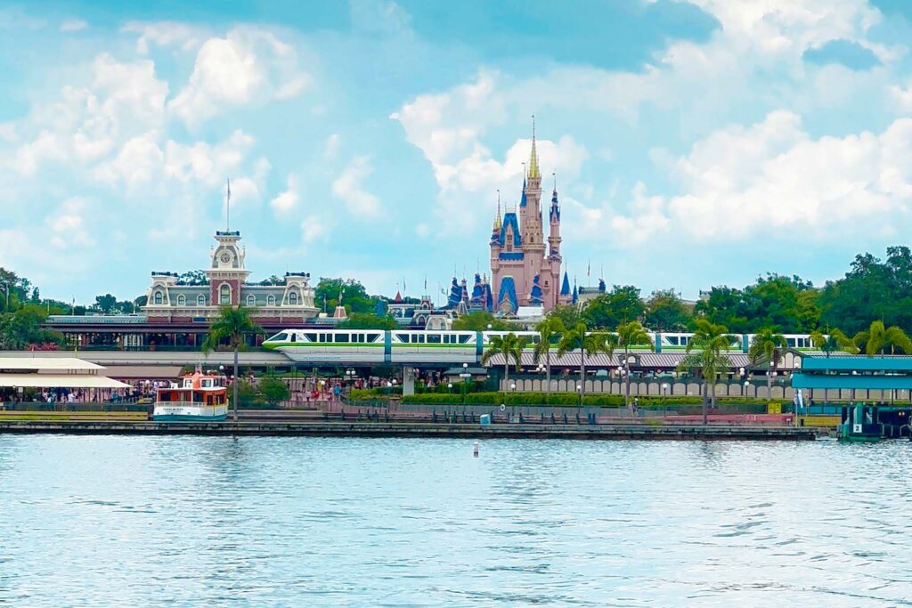 water in the foreground with the monorail running on a track in front of Magic Kingdom castle.