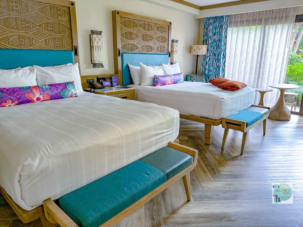 two queen beds with white coverlet and turquoise accents at Polynesian Village resort at Disney World.