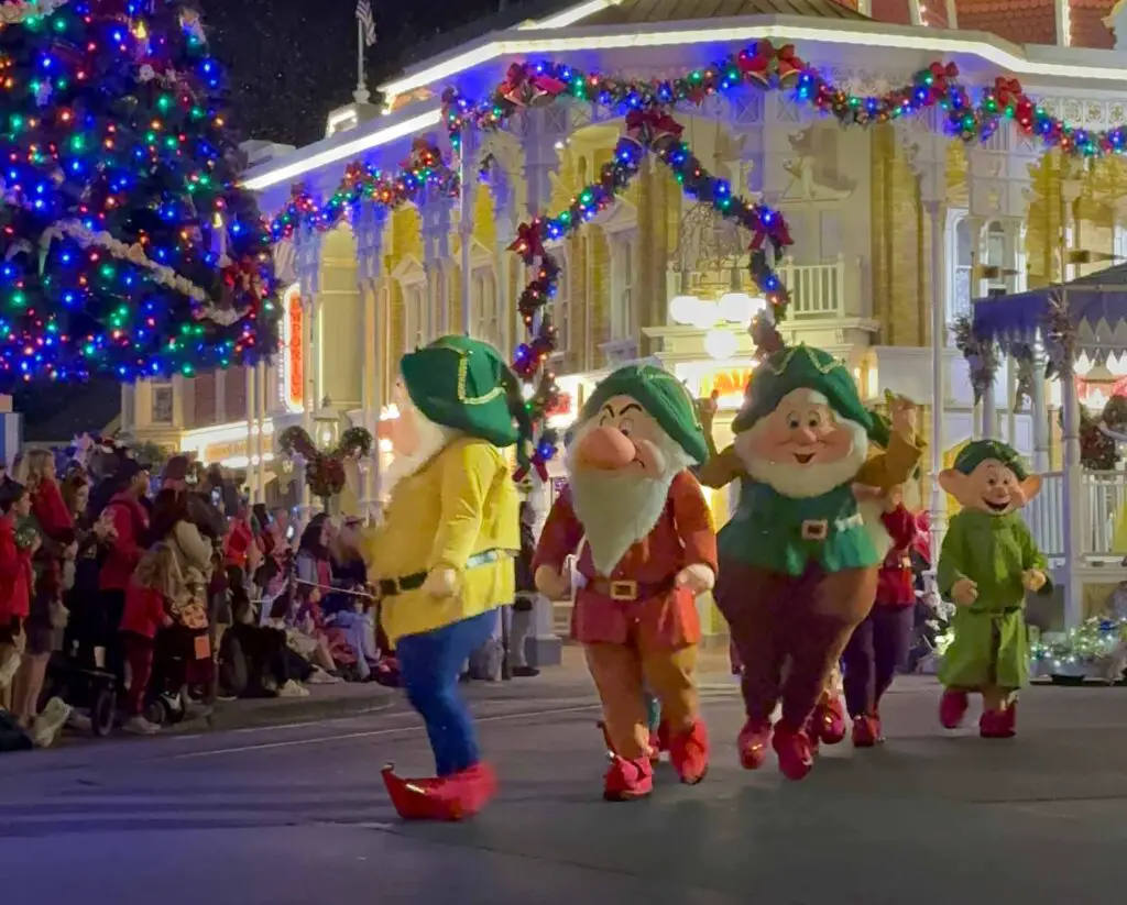 The 7 Dwarfs walk down Main Street USA, lit up with Christmas Lights, during Disney World's Christmas party.