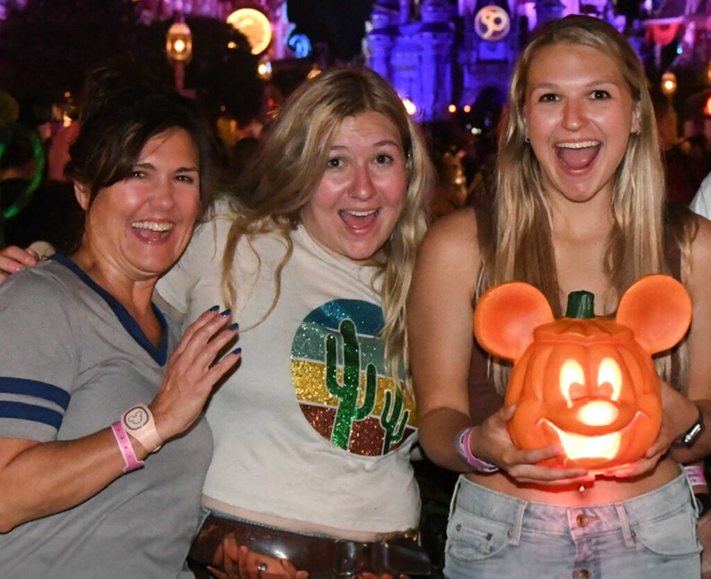 3 women pretend to be scared while holding a Mickey Mouse Jack-o-lantern in front of Cinderella Castle at Halloween