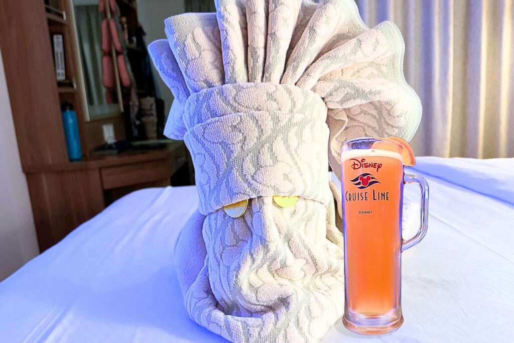 Towel creature on stateroom bed with a Disney Cruise beer mug.