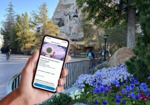 hand holding smartphone showing Disneyland Genie+ reservation in front of Matterhorn Bobsleds, a Disneyland Genie+ ride.