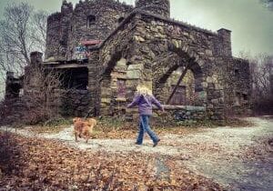 Young woman and golden retriever walk in front of Hearthstone Castle ruins